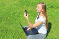 A beautiful young white girl in a white t-shirt and with long hair sitting on green grass, on the lawn and working behind a black Royalty Free Stock Photo