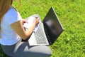 A beautiful young white girl in a white t-shirt and with long hair sitting on green grass, on the lawn and working behind a black Royalty Free Stock Photo