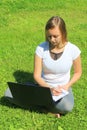 A beautiful young white girl in a white t-shirt and with long hair sitting on green grass, on the lawn and working Royalty Free Stock Photo