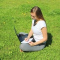 A beautiful young white girl in a white t-shirt and with long hair sitting on green grass, on the lawn and working behind a black Royalty Free Stock Photo