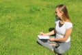 A beautiful young white girl in a white t-shirt and with long hair sitting on green grass, on the lawn and writes with a pen in a Royalty Free Stock Photo