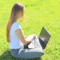 A beautiful young white girl in a white t-shirt and with long hair sitting on green grass, on the lawn and working behind a black Royalty Free Stock Photo