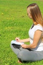 A beautiful young white girl in a white t-shirt and with long hair sitting on green grass, on the lawn and writes with a pen in a Royalty Free Stock Photo