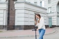 Beautiful, young, and white-toothed girl with long brown hair stopped while riding the scooter, to write to a friend on the phone.
