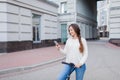 Beautiful, young, and white-toothed girl with long brown hair stopped while riding the scooter, to write to a friend on the phone.