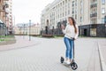 Beautiful, young, and white-toothed girl with long brown hair stopped while riding the scooter, to write to a friend on the phone.