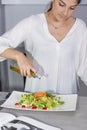 Beautiful young woman adding olive oil to a freshly made salad on a white plate at the kitchen