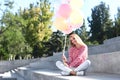 Beautiful young woman with air balloons sitting on stairs outdoors Royalty Free Stock Photo