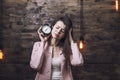 Beautiful young woman with alarm clock in hand and a sour face t