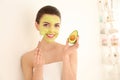 Beautiful young woman applying avocado facial mask in bathroom