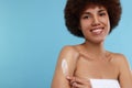 Beautiful young woman applying body cream onto arm on light blue background, space for text Royalty Free Stock Photo