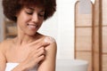 Beautiful young woman applying body cream onto shoulder in bathroom, space for text Royalty Free Stock Photo