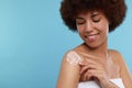 Beautiful young woman applying body cream onto shoulder on light blue background, space for text Royalty Free Stock Photo