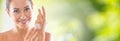 Beautiful young woman applying cream to her hand. Skincare spa wellness and cosmetics concept. Blurred green panoramic banner