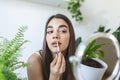 Beautiful young woman applying lip gloss with applicator in front of a mirror at home Royalty Free Stock Photo