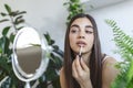 Beautiful young woman applying lip gloss with applicator in front of a mirror at home Royalty Free Stock Photo