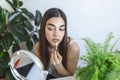 Beautiful young woman applying lip gloss with applicator in front of a mirror at home Royalty Free Stock Photo