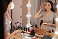 Beautiful young woman applying makeup near mirror in room Royalty Free Stock Photo