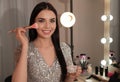 Beautiful young woman applying makeup near mirror in room Royalty Free Stock Photo