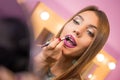 Beautiful young woman applying makeup, putting on lip liner and holding mirror Royalty Free Stock Photo