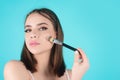 Beautiful young woman applying makeup on studio background. Pretty girl holding makeup brushes and make up on face with Royalty Free Stock Photo