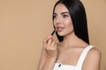 Beautiful young woman applying nude lipstick on beige background, space for text Royalty Free Stock Photo