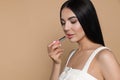 Beautiful young woman applying nude lipstick on beige background, space for text Royalty Free Stock Photo