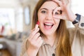 Beautiful young woman applying red lipstick with happy face smiling doing ok sign with hand on eye looking through fingers Royalty Free Stock Photo