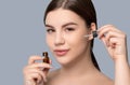 A beautiful young woman is applying a skin moisturizing serum to her face with a pipette. Cosmetology and professional skin care