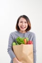 Beautiful young woman in apron holding paper shopping bag full of fresh vegetables and smiling Royalty Free Stock Photo