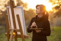 Beautiful young woman artist painting a picture on the easel, girl figure with a brush and a palette of colors on the background Royalty Free Stock Photo