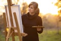 Beautiful young woman artist painting a picture on the easel, girl figure with a brush and a palette of colors on the background Royalty Free Stock Photo