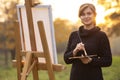 Beautiful young woman artist painting a picture on the easel, girl figure with a brush and a palette of colors on the background Royalty Free Stock Photo