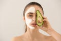 Beautiful young woman with avocado facial mask on light background