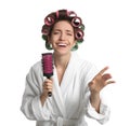 Beautiful young woman in bathrobe with hair curlers singing into hairbrush on white background Royalty Free Stock Photo