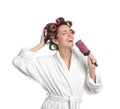 Beautiful young woman in bathrobe with hair curlers singing into hairbrush on white background Royalty Free Stock Photo