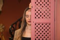 Beautiful young woman behind a pink wooden window cover. The woman is sad and looks at the ground with sorrow and depression Royalty Free Stock Photo