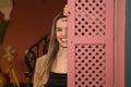 Beautiful young woman behind a pink wooden window cover. The woman is happy and looks at the camera Royalty Free Stock Photo