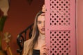 Beautiful young woman behind a pink wooden window cover. The woman is sad and looks at the camera Royalty Free Stock Photo