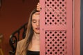 Beautiful young woman behind a pink wooden window cover. The woman is sad and looks at the ground with sorrow and depression Royalty Free Stock Photo