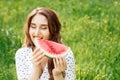 Beautiful young woman is biting slice of watermelon on grass background Royalty Free Stock Photo