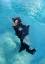 Beautiful young woman in black dress, dark brown curly hair floating fan-shaped in turquoise water Royalty Free Stock Photo