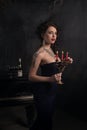 Beautiful young woman in black dress next to a piano with candelabra candles and wine, dark dramatic atmosphere of the castle.