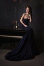 Beautiful young woman in black dress next to a piano with candelabra candles and wine, dark dramatic atmosphere of the castle.