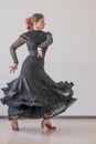 Beautiful young woman in a black elegant dress and a red flower in her hair is dancing flamenco on a background of a gray wall Royalty Free Stock Photo