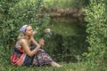 A beautiful young woman with blond hair in a sundress on the shore of a lake with a bouquet of wildflowers. National Russian Royalty Free Stock Photo