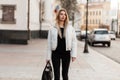 Beautiful young woman with blond hair in a trendy white jacket in jeans with a black stylish leather bag on the street. Attractive Royalty Free Stock Photo