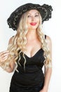 Beautiful young woman blonde in black dress and hat with decollete.