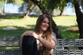 Beautiful young woman with blonde hair and blue eyes sits on park bench and poses for photo like a model. She is happy doing Royalty Free Stock Photo