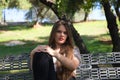 Beautiful young woman with blonde hair and blue eyes sits on park bench and poses for photo like a model. She is happy doing Royalty Free Stock Photo